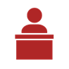 A simple red icon depicting a person standing behind a podium.